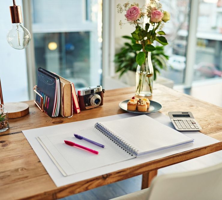 Virtual Assistant. Amber Assists. Desk neatly organized wooden with camera and pink and purple pen with pin flowers and cupcakes on desk