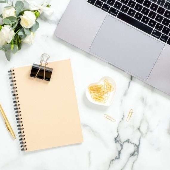 Virtual Assistant. AmberAssists. Laptop on marble desk with flowers and a notebook and paperclips